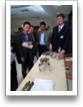 R. Sedaghat (M) and other visitors watch G. McVittie (R) demonstrate a model of an Actively Stabilized Tetrapod Robot.